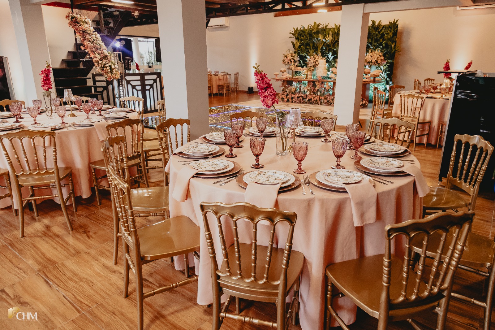 Mesas redondas com decoração em tons rosê e cadeiras douradas